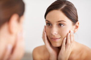 Woman smiles in the mirror, touching her smooth, youthful-looking skin after Morpheus8 microneedling